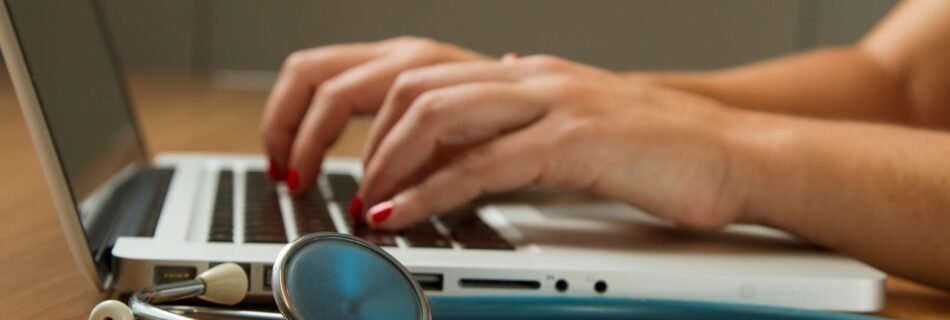 person sitting while using laptop computer and green stethoscope near